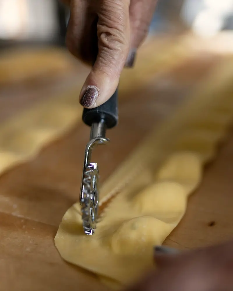 Eine Hand schneidet mit einem gezackten Teigrad gefüllte Ravioli aus einer Teigbahn