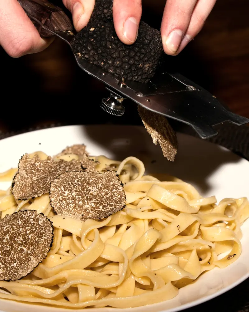 Mit einem Trüffelhobel werden dünne Scheiben Trüffel über einen Teller Tagliatelle gehobelt