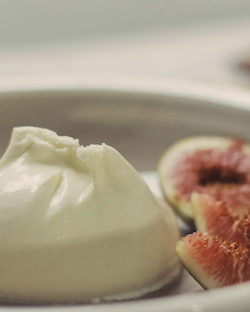 Burrata in einer hellen Keramikschale, daneben aufgeschnittene frische Feigen