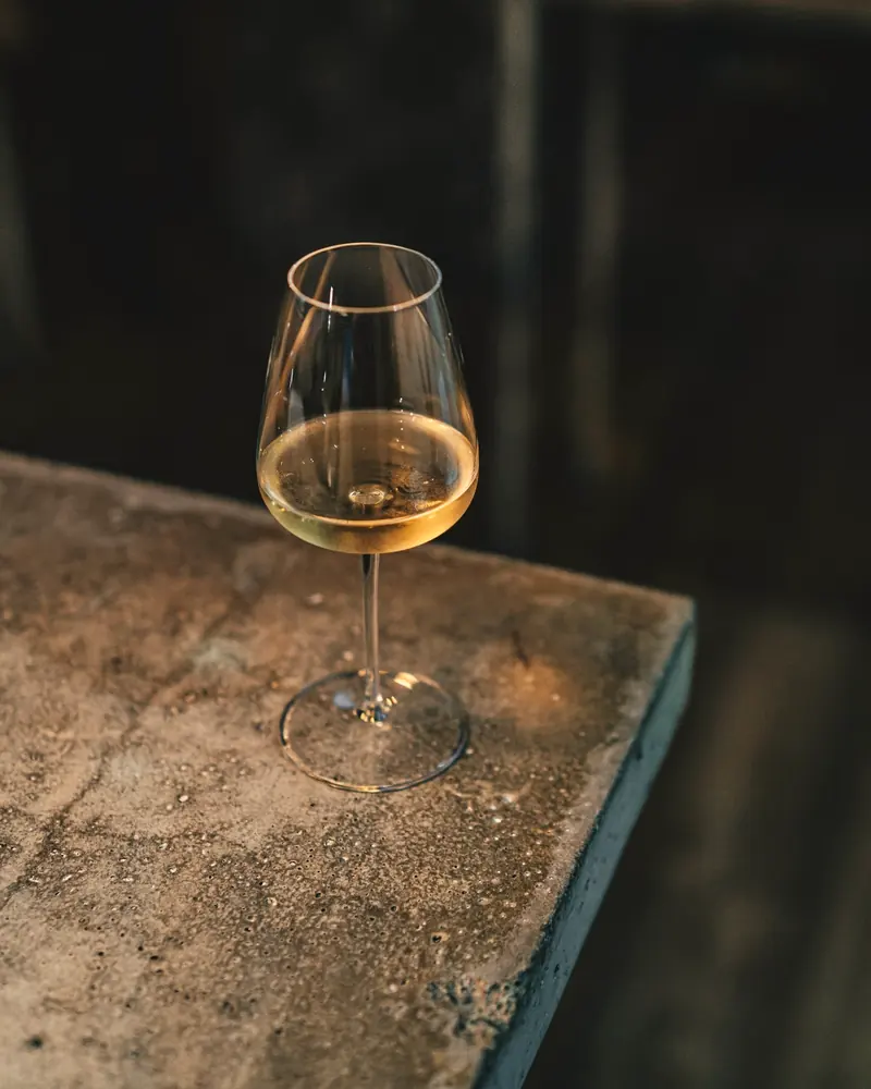 Ein Glas goldgelber Orange-Wein auf einem alten Steintisch in warmem Licht
