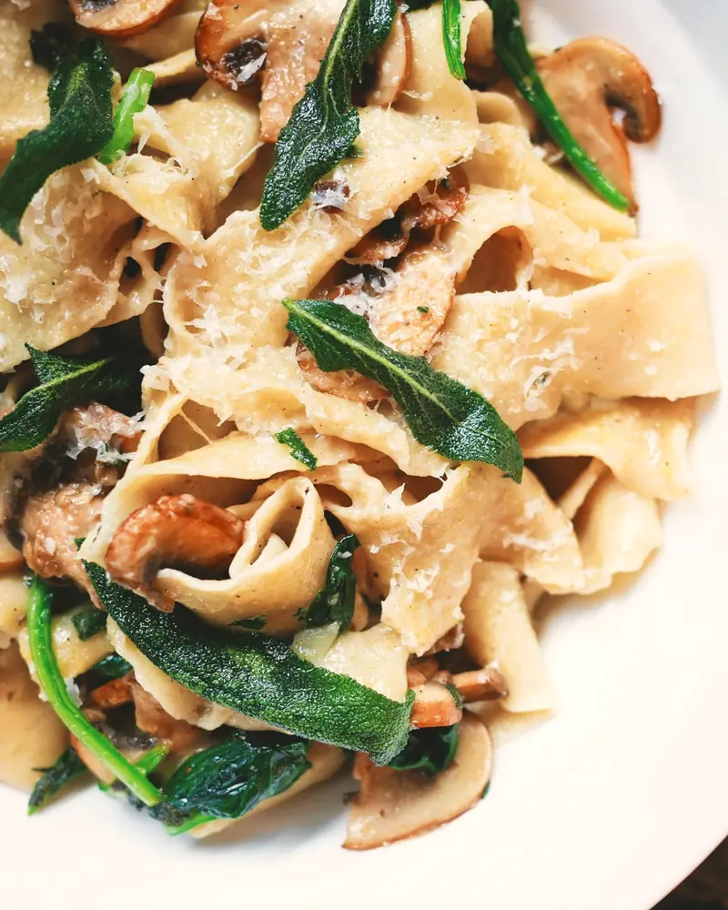 Pappardelle mit Steinpilzen, frittierten Salbeiblättern und geriebenem Pecorino in einem weißen Teller, von oben fotografiert