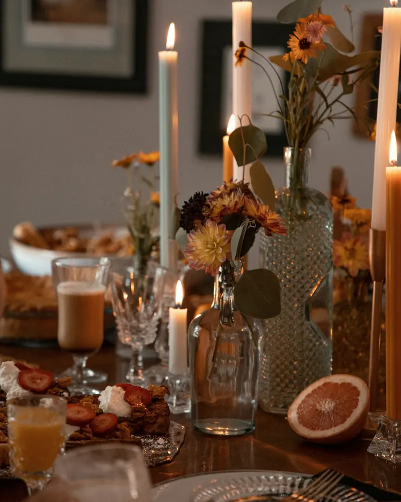 Festlich gedeckter Tisch mit hohen Kerzen, Herbstblumen in Glasflaschen und Kristallgläsern